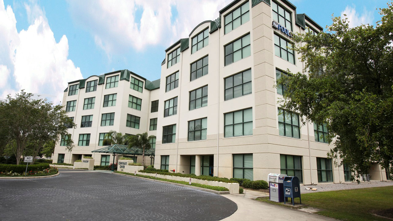 Modern office building, three-story, paved driveway, large windows, green landscaping.