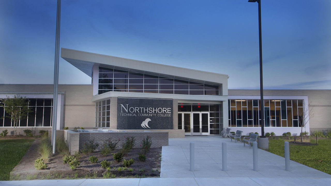 Northshore Technical Community College building entrance with flag, benches, and landscaped grounds.